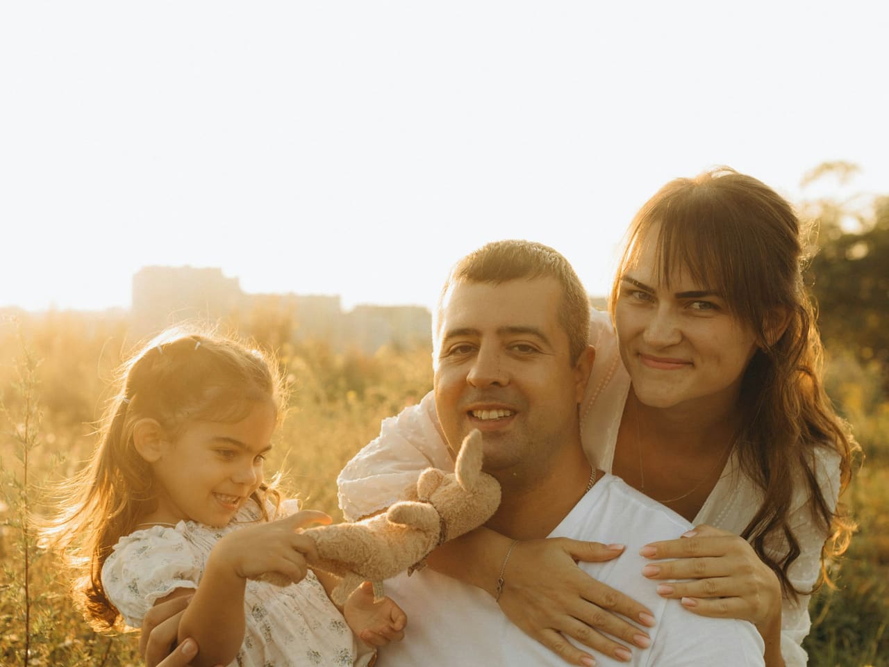 Pai, mãe e filha abraçados, sorrindo